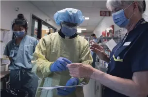  ?? JONATHAN HAYWARD THE CANADIAN PRESS ?? Rev. Victor Fernandes puts on protective gear prior to visiting with a patient in the COVID-19 intensive care unit at St. Paul’s hospital in Vancouver on Tuesday.