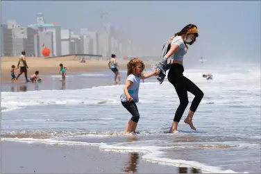  ?? (AP Photo/Steve Helber, File) ?? Victoria Faughnan, right, and Evelyn Faughnan play in the surf May 22 in Virginia Beach, Va., the day the state reopened the beachfront after the coronaviru­s lockdown. The pandemic not only has upended the tourism industry, but also how states, cities and attraction­s market themselves as summer travel destinatio­ns.