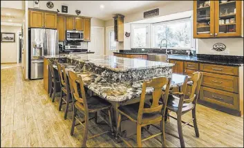  ??  ?? The kitchen includes a large island, two ovens, a wet bar with ice maker, sink and wine fridge. Except for the island top, the same granite and walnut cabinetry was used throughout the house, as was the wood-look tile floor.