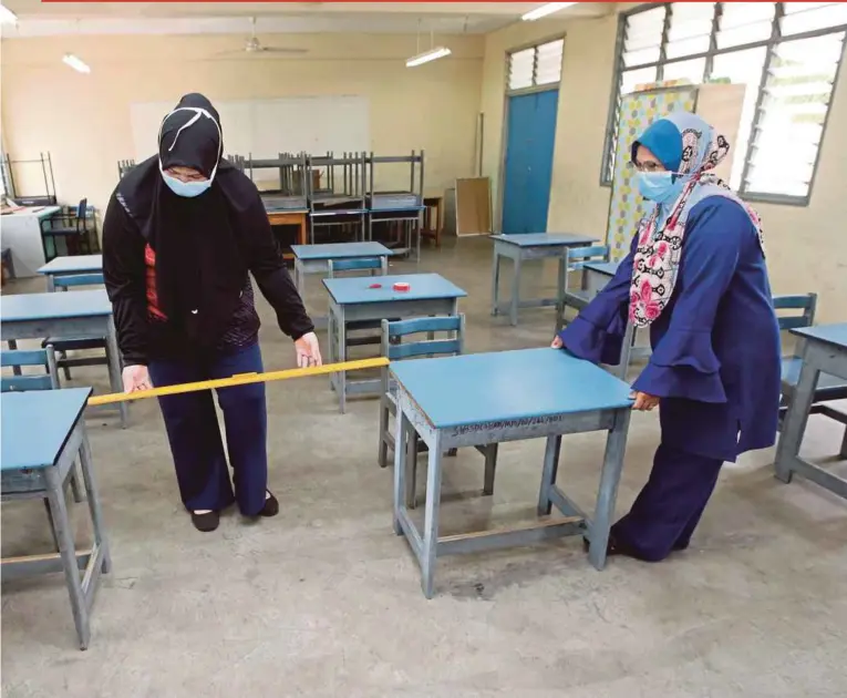  ?? PIC BY EIZAIRI SHAMSUDIN ?? School staff members measuring the gap between two desks to allow for social distancing at a primary school in Kuala Lumpur.