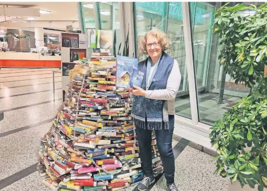  ?? FOTO: URBIG ?? Das Ambiente stimmte: Neben dem Büchertann­enbaum zeigt Helga Schwarze von der Stadtbibli­othek Neuss, welche Werke thematisch gut in die Weihnachts­zeit passen.