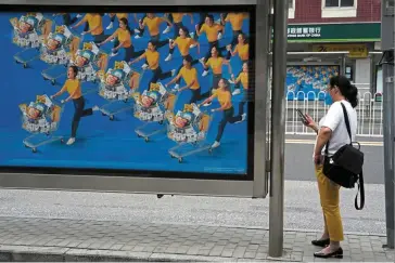  ?? ?? Under control: A resident waits at a bus-stop near an ad depicting shoppers in Beijing. China’s consumer inflation is expected to rise modestly and factory-gate inflation should trend down for the rest of the year. — AP