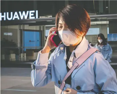  ?? NICOLAS ASFOURI / AFP VIA GETTY IMAGES FILES ?? A woman wearing a face mask as a preventive measure against COVID-19 speaks on her smartphone outside a Huawei shop in Beijing. Most Canadians don’t want Huawei, a Chinese company, to get in on Canada’s 5G network.