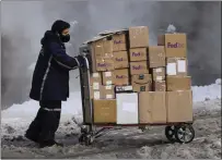  ?? Bloomberg photo by Angus Mordant ?? A driver for an independen­t contractor to FedEx Corp. pushes a cart of packages through snow in New York on Dec. 17, 2020.