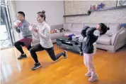  ??  ?? Dino Lin, Stella Zhang and Wowo Lin, 5, exercise using filled water bottles as weights as they watch a fitness video at their house in Shanghai.