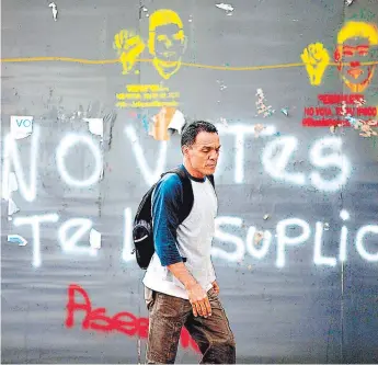  ?? FOTO: AGENCIA AP ?? Un hombre camina por las calles de Caracas después de una marcha de protesta en la que opositores pintaron las paredes pidiendo a la población que se abstenga de participar en elecciones.