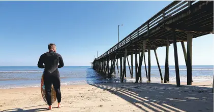  ?? THE’ N PHAM/STAFF ?? Zach Bowman waits for the right wave for skimboardi­ng near the Virginia Beach Fishing Pier last week. The pier is being prepared for a spring reopening.