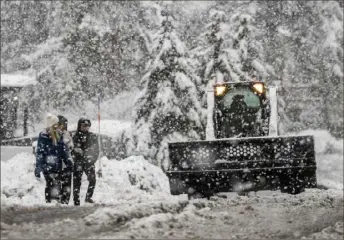  ?? Stephen Lam/San Francisco Chronicle via AP ?? Pedestrian­s walk along a road Saturday as a snowplow works in South Lake Tahoe, Calif. Residents in parts of Northern California were ordered to evacuate because of flooding.