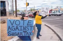  ??  ?? Patsy Sisneros-Walters, left, and Lisa Medina-Lujan hold signs opposing a tax on sugary drinks at Osage and Cerrillos on election day Tuesday.