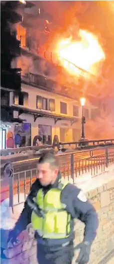  ??  ?? A first responder arrives as the fire rages, left. Right: Firefighte­rs examine the charred remains of the building following yesterday’s inferno