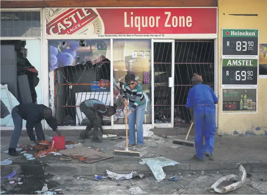  ?? Picture: Reuters ?? DAMAGE. People clean up in front of a liquor store that was damaged and looted during violent demonstrat­ions in Coligny, North West. The protest action was sparked by the death of a boy.