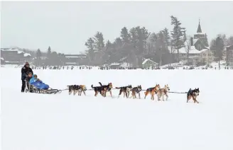  ?? AP ?? John Houghton of Vermontvil­le, N.Y., and his sled dog team give a ride to a couple around Mirror Lake in Lake Placid, N.Y. For a closer mush, the sport is popular in Ely, Minn.