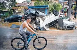  ?? CARL DE SOUZA/GETTY-AFP ?? A bicyclist on Wednesday makes his way past cars destroyed by a flash flood in Petropolis, Brazil. Officials said the area received 10 inches of rain Tuesday.