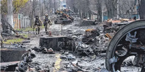  ?? FOTO: RODRIGO ABD/DPA ?? Verwüstung vor den Toren Kiews: Zwei ukrainisch­e Soldaten gehen in Butscha eine Straße mit zerstörten russischen Militärfah­rzeugen entlang.