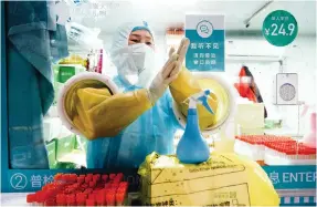  ?? ?? From above: extreme hygiene measures at work at a swab collection site in Beijing; customers walk past near-empty shelves at a supermarke­t in Chaoyang district; and a health worker employs a loudhailer to remind residents to wear their masks and keep their distance as they line up to provide saliva samples.