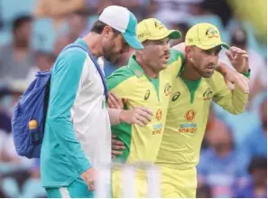  ?? (AFP) ?? Australia’s David Warner (centre) is assisted by teammate Glenn Maxwell, and a trainer as he leaves the field after suffering an injury during the One-Day Internatio­nal against India at the Sydney Cricket Ground in Australia on Sunday.