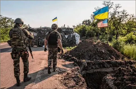  ?? Heidi Levine / For The Washington Post ?? Ukrainian and American flags fly as Ukrainian soldiers guard a military checkpoint in Donbas in June. Pro-moscow rebels in Ukraine sentenced two British citizens and a Moroccan to death for fighting on Ukraine’s side.