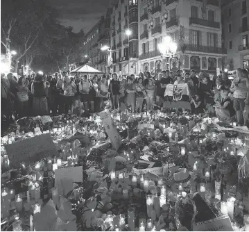  ?? EMILIO MORENATTI / THE ASSOCIATED PRESS ?? Mourners gather at a memorial on Barcelona’s Las Ramblas promenade to the victims of Thursday’s terror attacks that killed 14 people. Spanish police on Friday killed five people during a later attack 100 kilometres to the south.