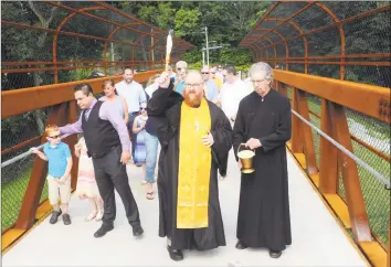  ?? Ned Gerard / Hearst Connecticu­t Media ?? Rev. Patrick Burns from Three Saints Orthodox Church, in Ansonia, is joined by others as he blesses the pedestrian bridge leading to the newly completed section of the Ansonia Riverwalk Park, in Ansonia on Aug. 8. The bridge spans the rail tracks next to Pershing Drive, and now connects the Naugatuck River Greenway to pedestrian and bicycle traffic south through Ansonia, Derby and Shelton.