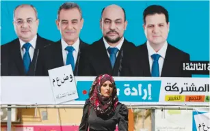  ?? (Ammar Awad/Reuters) ?? A WOMAN walks past a campaign billboard for the Joint (Arab) List in Umm el-Fahm yesterday.