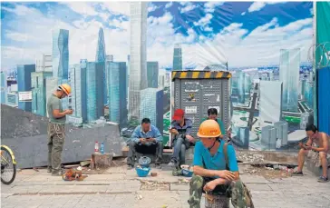  ?? EPA-EFE ?? Constructi­on workers relax in front of a banner showing the Central Business District in Beijing. China’s economy appears to be showing signs of further cooling as tougher US tariffs loom and investment in the first seven months of the year slow to a record low, according to data released by the National Bureau of Statistics yesterday.