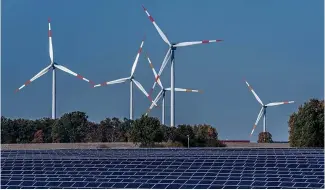  ?? ?? Des éoliennes tournent derrière un parc solaire à Rapshagen, en Allemagne.