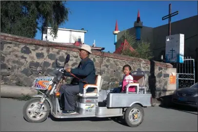  ?? The Associated Press ?? CHANGBAI: In this Aug. 30, 2017, photo, a man give a child a ride past a cross at what used to be the site of a church in the Chinese border town of Changbai in northeaste­rn China’s Jilin province. Some missionari­es in northeaste­rn China are engaged in a dangerous work: spreading Christiani­ty across the border to North Korea. A South Korean pastor says at least 10 such front-line missionari­es and pastors have died mysterious­ly in recent years.