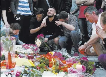  ?? JENS MEYER/THE ASSOCIATED PRESS ?? People mourn behind flower tributes near the Olympia shopping center in Munich on Saturday, a day after a shooting there left nine people dead. Police piecing together a profile of the gunman described him as a lone, depression-plagued teenager.