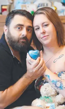  ??  ?? Courtney and Ben Burvill hold their stillborn son Atreus’s ashes in a heart-shaped urn, Picture: Glenn Hampson