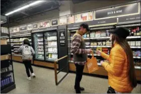  ?? ELAINE THOMPSON — THE ASSOCIATED PRESS FILE ?? A worker, right, looks at the ID of a shopper at the wine and beer area inside an Amazon Go store in Seattle. Get ready to say good riddance to the checkout line.