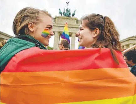  ?? Tobias Schwarz, AFP/Getty Images ?? Two women wrap themselves in a rainbow flag during a rally of gays and lesbians in front of the Brandenbur­g Gate in Berlin on Friday, the day that the German parliament legalized same-sex marriage.