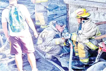  ?? MACKY LIM ?? BROTHERHOO­D. A firefighte­r sprays water on his buddy after putting out the fire at Purok 26, Muslim Village, Times Beach in Matina, Davao City that razed 50 houses.