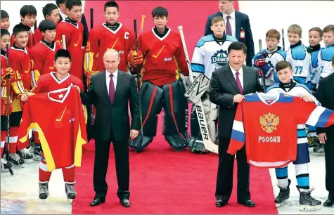  ?? WU ZHIYI / CHINA DAILY ?? President Xi Jinping and Russian President Vladimir Putin exchange team uniforms and take a group photo with the players participat­ing in a friendly Sino-Russian youth ice hockey game in Tianjin on Friday.