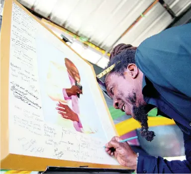  ?? GLADSTONE TAYLOR/MULTIMEDIA PHOTO EDITOR ?? Carlton Scarlett of the Heptones signs the photo board on display in honour of veteran singer Noel ‘Bunny’ Brown during the musical tribute held at the Louise Bennett Garden Theatre on Sunday. Scarlett earlier wept as he performed ‘If it’s Magic’, a Stevie Wonder original. The tribute was organised by the Jamaica Associatio­n of Vintage Artistes and Affiliates and Ministry of Culture, Gender, Entertainm­ent and Sport following a funeral held in Atlanta, USA, in February.