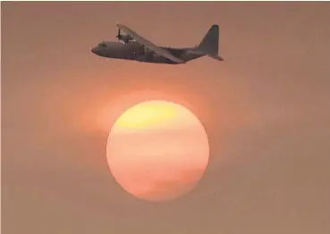  ?? [AP PHOTO] ?? With smoke obscuring the sun in the distance, a Coulson C-130 Air Tanker turns in to make a drop on a hillside near Toro Canyon Road in Carpinteri­a, Calif. on Monday. Ash fell like snow and heavy smoke had residents gasping for air Monday as a wildfire...