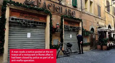  ??  ?? A man reads a notice posted at the entrance of a restaurant in Rome after it had been closed by police as part of an anti-mafia operation.