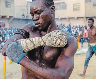  ?? NEW YORK TIMES FILE PHOTO ?? Boxer Tijjani Zakari wraps his arm in cord before a fight in the Nigeria Traditiona­l Boxing League season finals in Kano, Nigeria, in April. Dambe, a generation­s-old West African style of boxing, is making a comeback.
