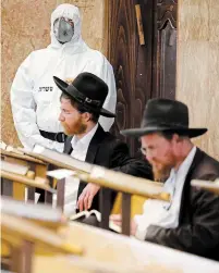  ?? ARIEL SCHALIT THE ASSOCIATED PRESS ?? An Israeli police officer wearing protective gear waits to detain ultra-Orthodox men as they pray in a synagogue in defiance of the government’s COVID-19 guidelines in Bnei Brak on Thursday.