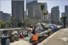  ?? AP PHOTO/RICHARD VOGEL ?? A homeless man sits at his street side tent along the Interstate 110 freeway along downtown Los Angeles’ skyline on Thursday.