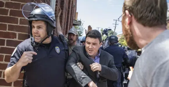  ?? EDU BAYER/THE NEW YORK TIMES ?? Police escort blogger Jason Kessler, the organizer of Saturday’s disastrous Unite the Right rally, away after he was confronted and punched Sunday at a news conference in Charlottes­ville, Va.