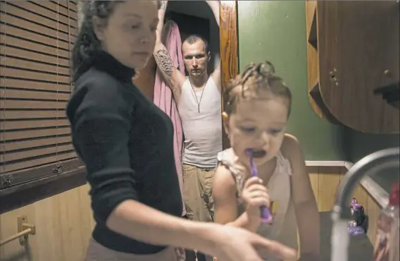  ??  ?? T.J. Ashbaugh stands in the doorway of the bathroom as his wife, Kate, helps her daughter, Emily, brush her teeth at their home in North Vandergrif­t.