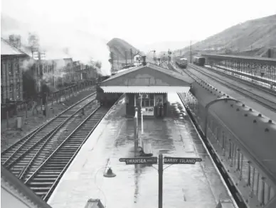  ?? Author’s Collection ?? Viewed from the footbridge at Treherbert station, the fingerboar­ds show the destinatio­ns to Swansea and Barry Island in 1960. To the right is the relatively new fuelling and servicing point for diesel-multiple-units, not far from the wider site of the first engine shed, and behind these sidings are the remains of Lady Margaret Colliery, which was in production until the early 1940s. The signal box at the far end of the island helps locate the spur to the second engine shed, which itself goes unseen behind a simmering steam locomotive and nearby housing. The mountain of colliery waste beyond the box is on the site of Ynysfeio Colliery, which by 1945 was only retained as a pumping station.