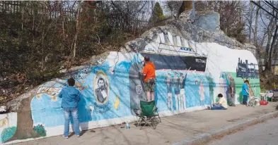  ?? Photos by Joseph B. Nadeau ?? Above and below: Retired Woonsocket High School art teacher Diane Mayers finishes up a Cass Ave mural on Monday with the help of volunteers from her Blackstone art studio. The mural tells the story of Charles Hays and his never finished Southern New England Railway.