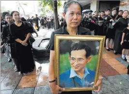  ?? Sakchai Lalit ?? The Associated Press A mourner holds a portrait of late Thai King Bhumibol Adulyadej while in line to pay respects outside the Grand Palace in Bangkok on Thursday. Adulyadej died on Oct. 13 last year at age 88 after seven decades on the throne.