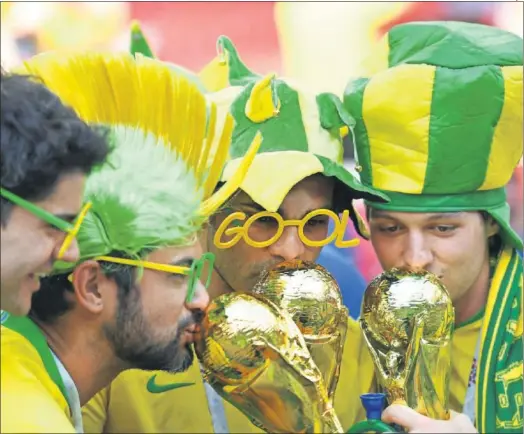  ??  ?? SOÑANDO EN ORO. Aficionado­s brasileños, besando réplicas de la Copa del Mundo.