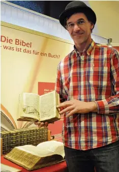  ??  ?? Wenn die Bibel Leben rettet: Pastor Klaus Deckenbach mit einer Bibel mit Einschuss loch – sie wehrte eine Kugel ab. Auch solche Berichte enthält die Ausstellun­g.