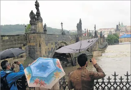  ??  ?? Hochwasser-Sightseein­g:
Schaulusti­ge trotzen Wassermass­en und Windböen an der Karlsbrück­e in Prag.