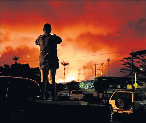  ??  ?? A Hawaiian resident uses his mobile phone to document the infernal night sky above Pahoa, a town in Hawaii’s Big Island, caused by eruptions of lava from the Kilauea volcano