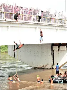  ?? — Reuters photo ?? Honduran migrants jump and climb down from the bridge that connects Mexico and Guatemala to avoid the border checkpoint as others look while queueing to enter Mexico, in Ciudad Hidalgo, Mexico.