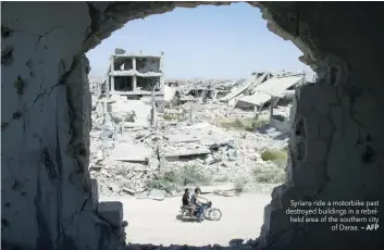  ?? — AFP ?? Syrians ride a motorbike past destroyed buildings in a rebelheld area of the southern city of Daraa.